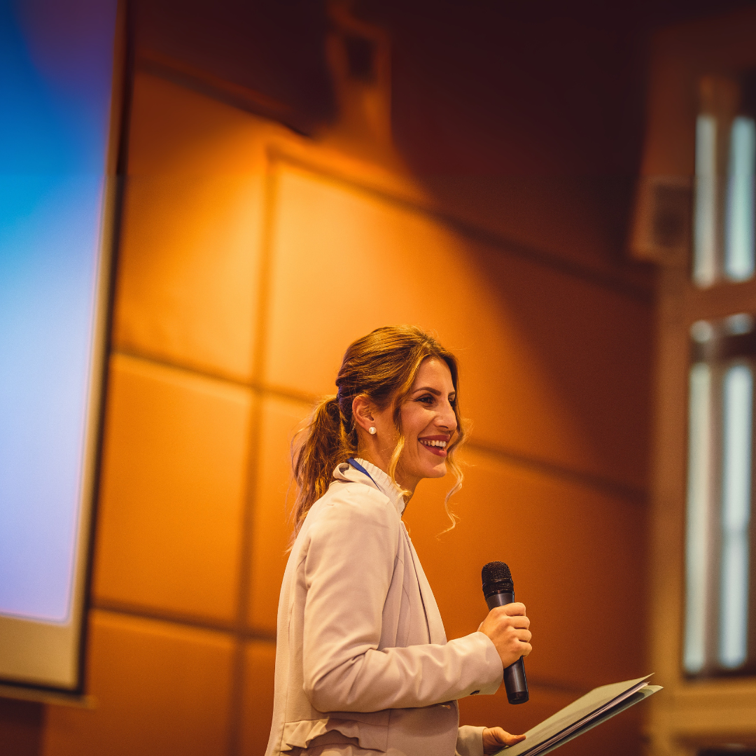 Confident speaker delivering a talk on stage, with a slide featuring their book cover behind them.